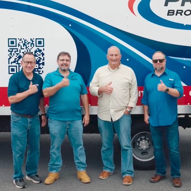 Four men stand in front of a branded truck, all giving thumbs up and smiling at the camera.